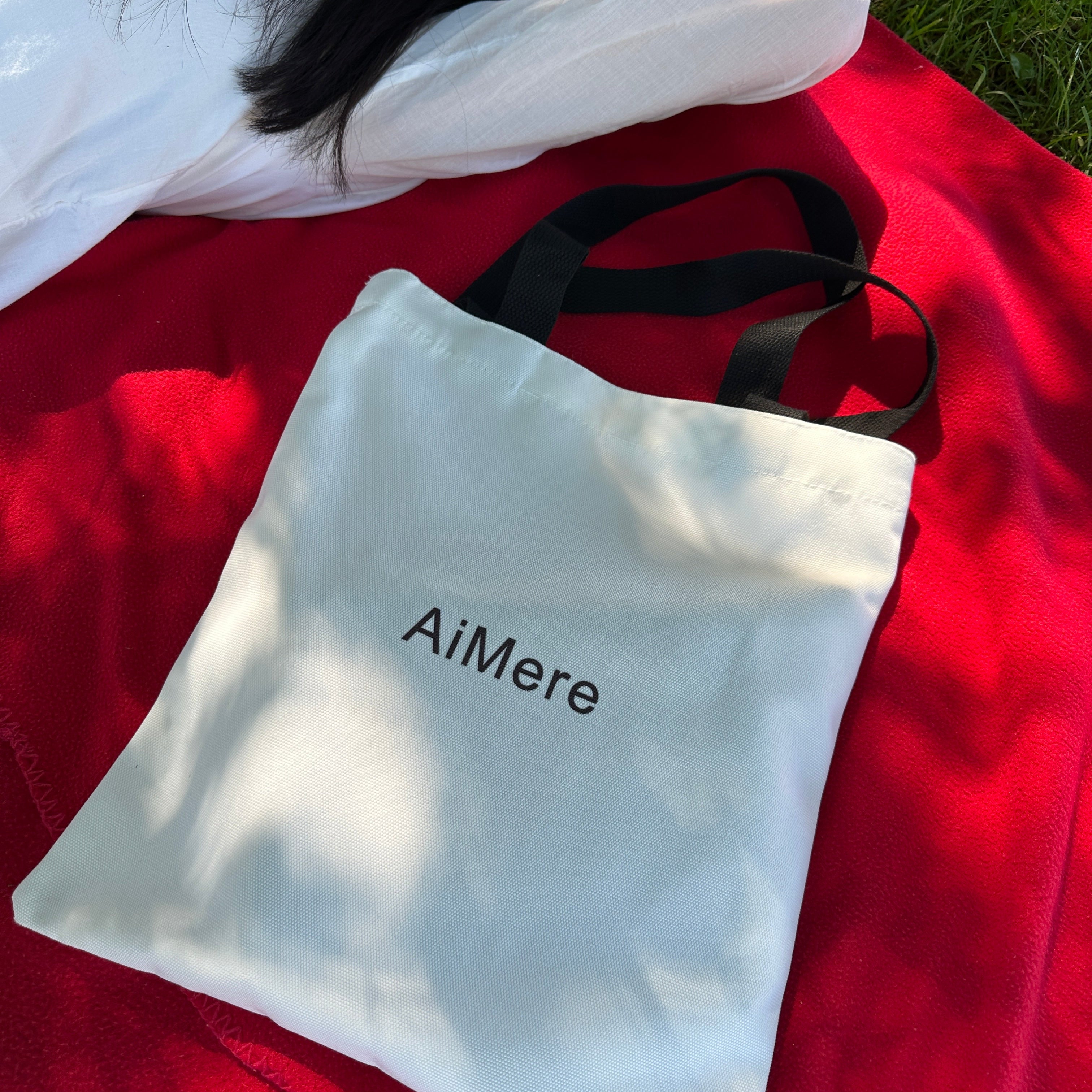 White bag with 'AiMere' branding on a red surface picnic tote bag