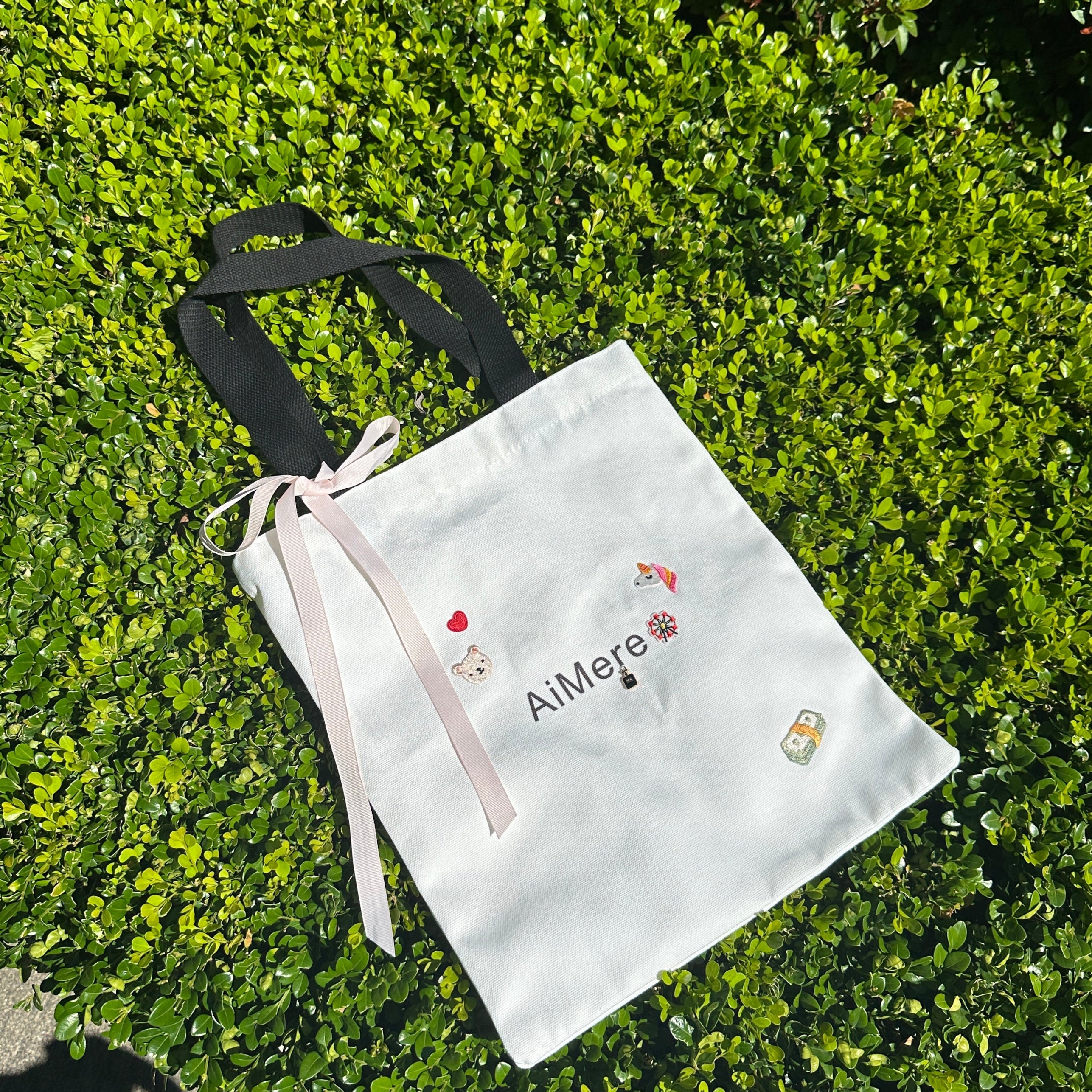 White drawstring bag with floral embroidery on a green bush