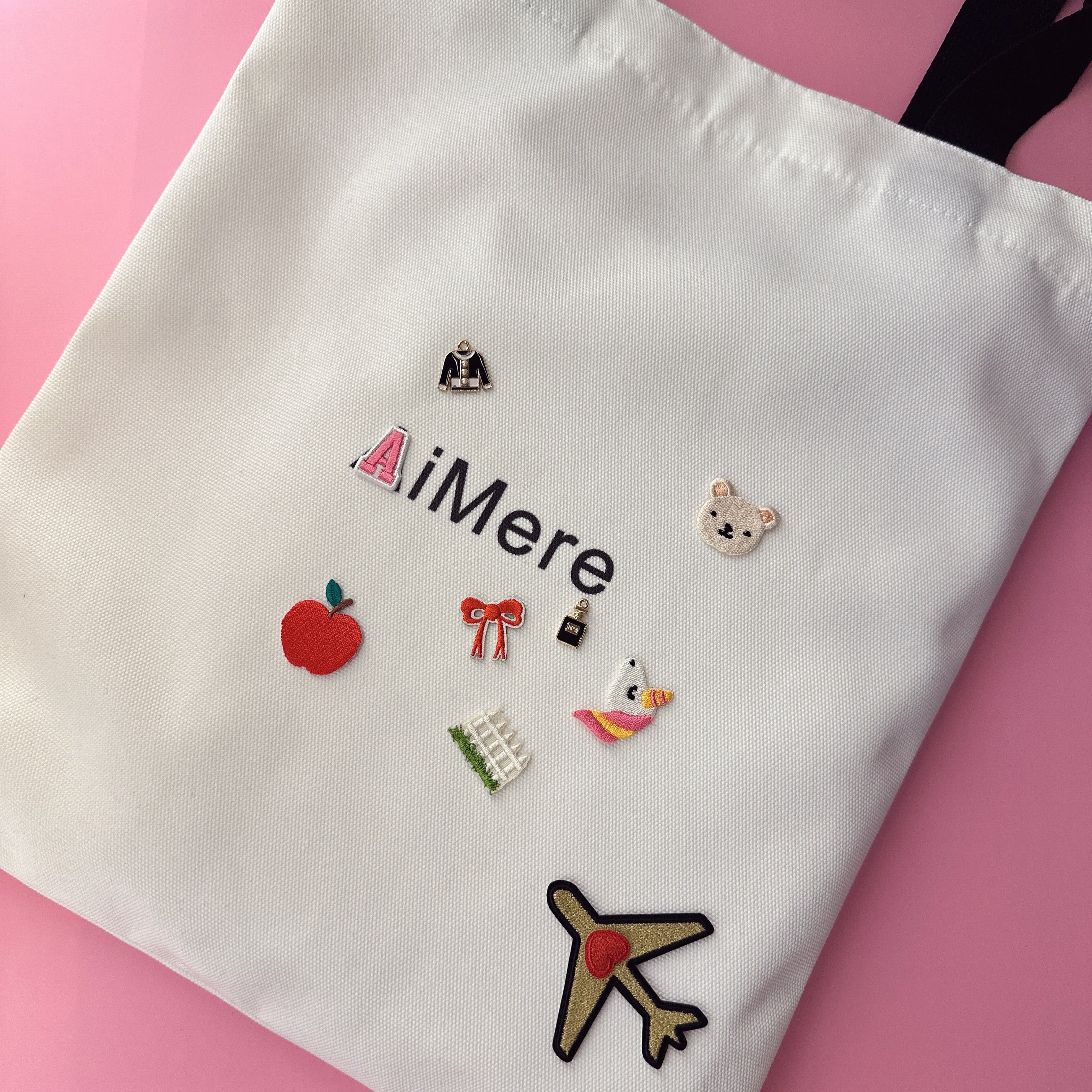 White tote bag with various patches on a pink background
canvas tote bag, customizable tote, AiMere tote, designer bag protection, everyday carry, DIY tote bag, travel tote, work bag, grocery tote