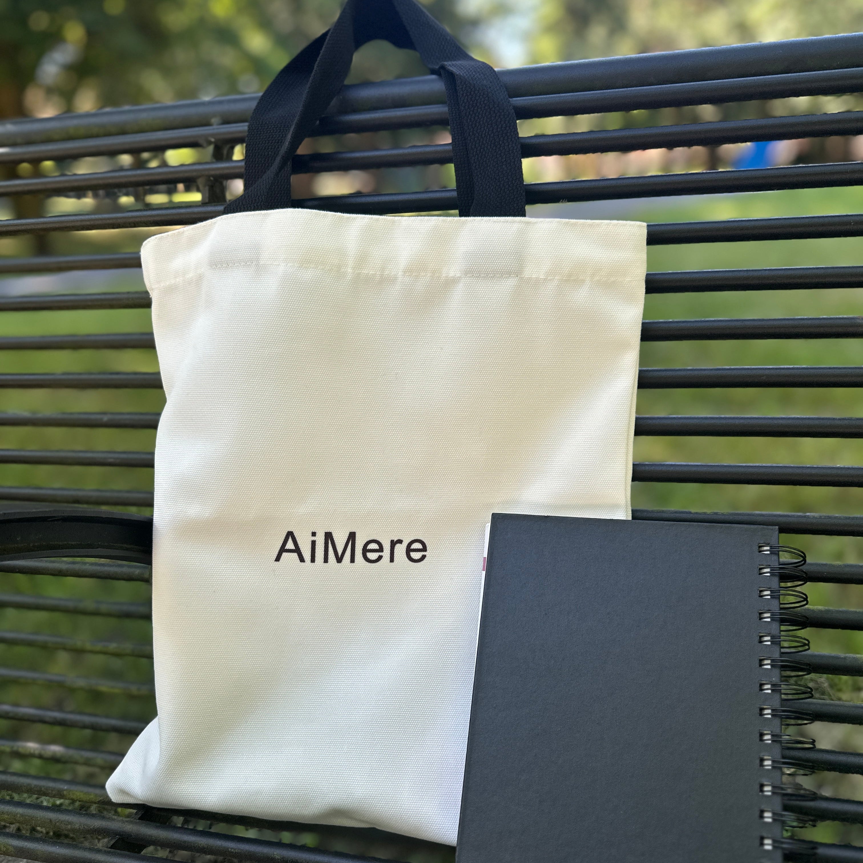 White tote bag with 'AiMere' branding on a black metal bench. Park tote bag