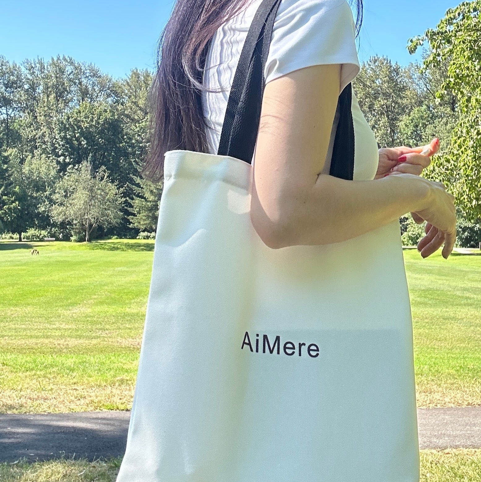 Person holding a white tote bag with 'AiMere' branding in an outdoor setting.