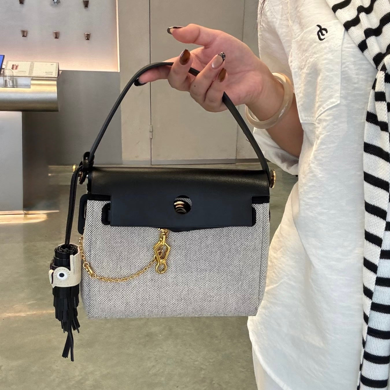 Person holding a top handle herbag with a black handle and gold chain detail.