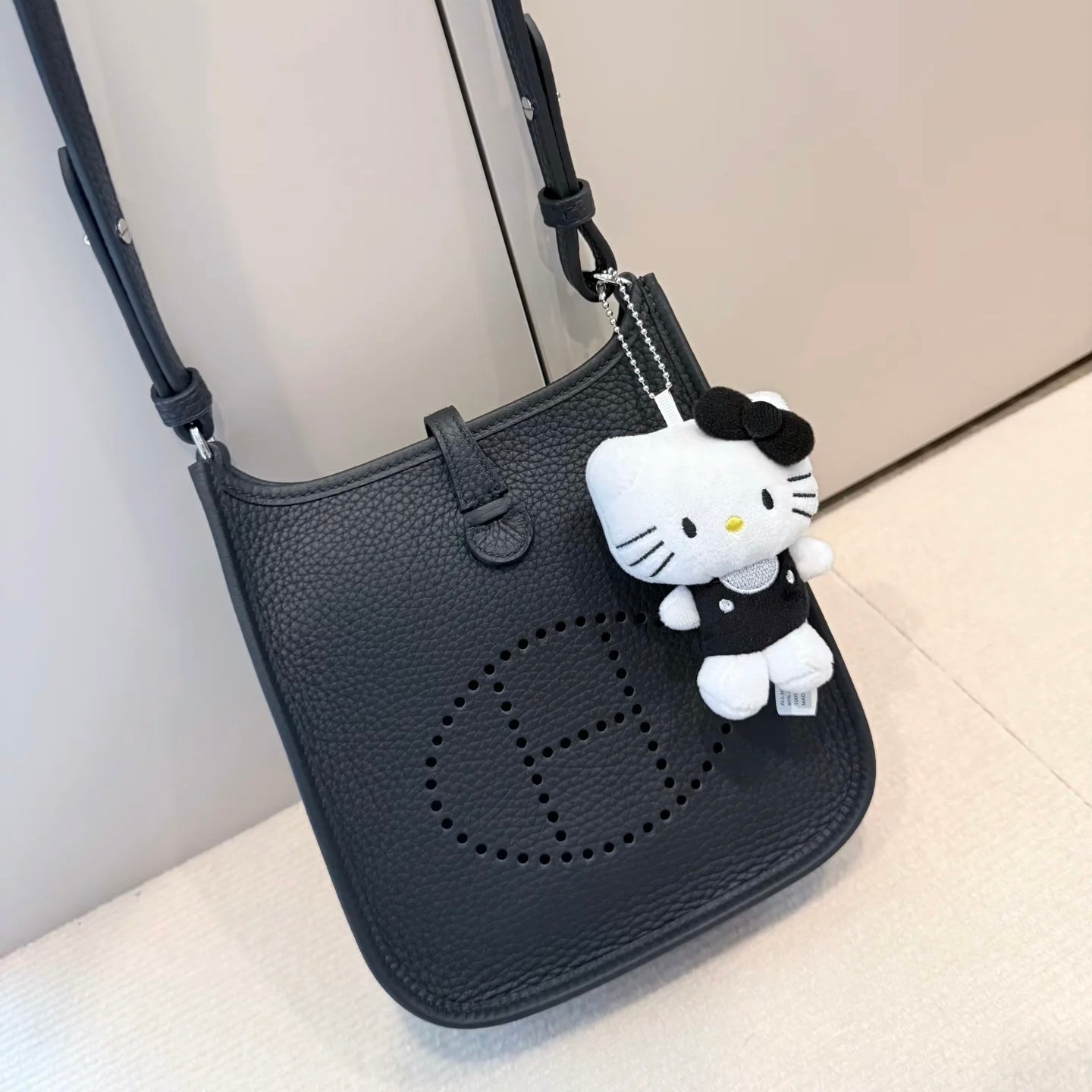 Black Hermes Evelyne handbag with a Hello Kitty charm on a light background