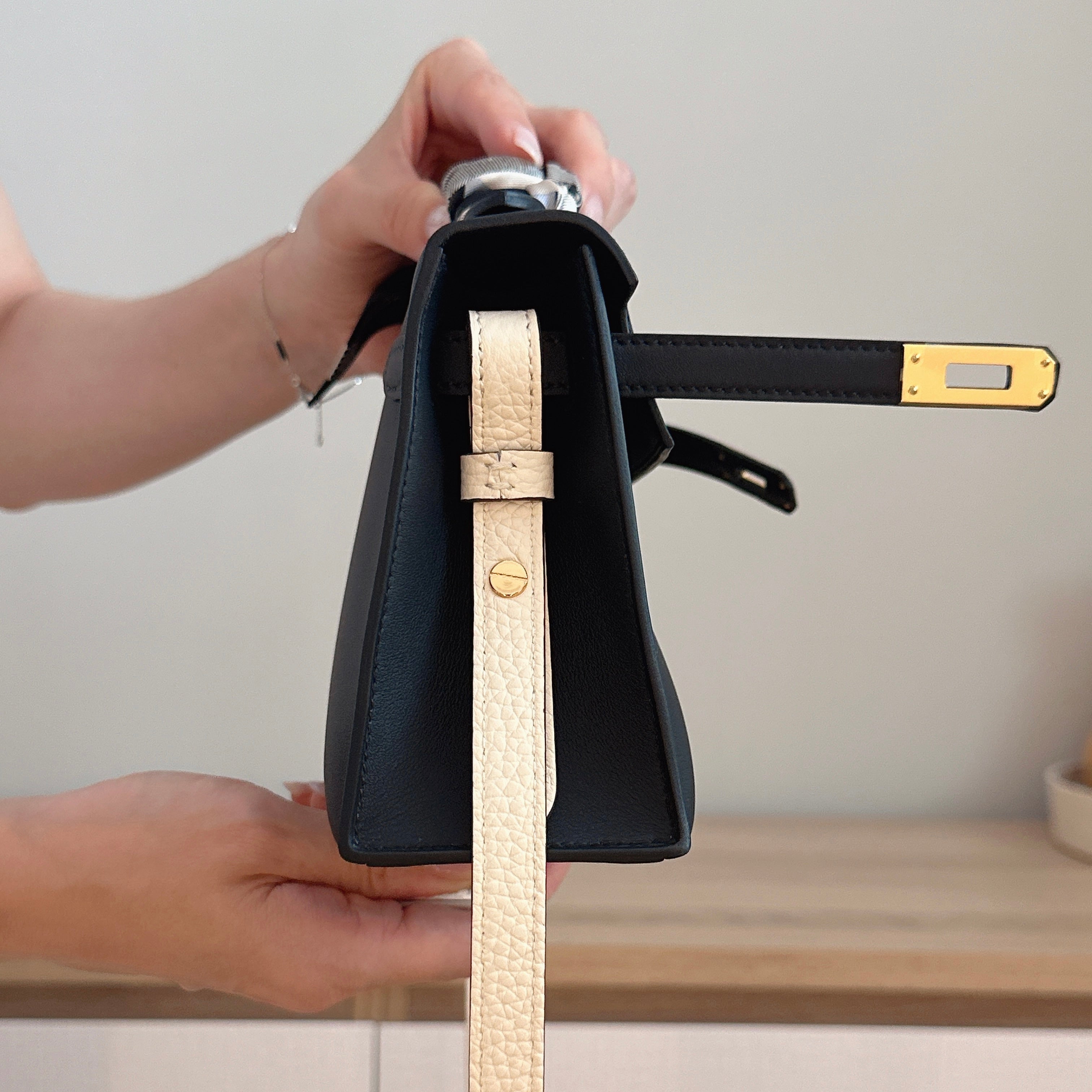 Person holding a black handbag with a gold strap against a neutral background