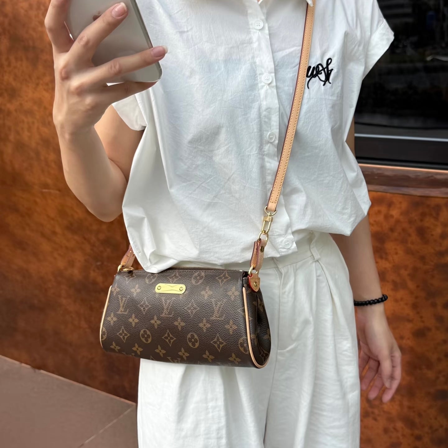 Person outfit pairing a white shirt and white pants, holding a smartphone and a LV crossbody.